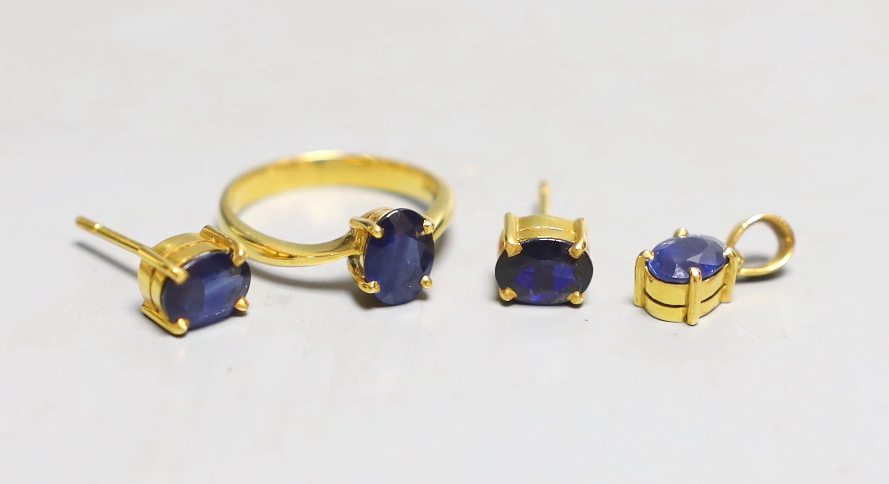 A modern suite of yellow metal and synthetic? sapphire set jewellery, comprising a ring, pendant and pair of earrings, the ring and pendant stamped 18k, gross 7.5 grams.